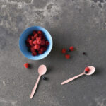 Raspberries in a blue bowl with pink spoons sit on top of Rugged Concrete quartz countertop.