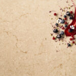 A red jam smear is surrounded by fresh berries and a silver spoon on Taj Royale quartz.