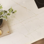 A plant sits on a countertop of crisp white Aterra Verity quartz interlaced with thin linear veins of bronze and copper.