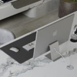 A computer sits on a desk of Calacatta Thyme ICON with translucent sage and gray veining accented by a dark green and white base.