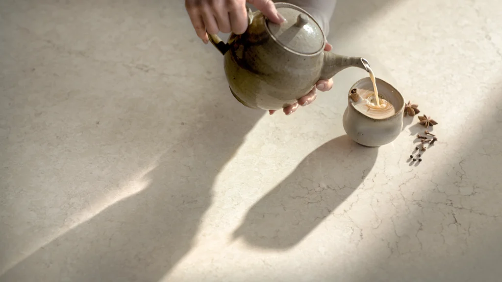 Hand pouring tea from a teapot into a cup beside star anise and cloves.